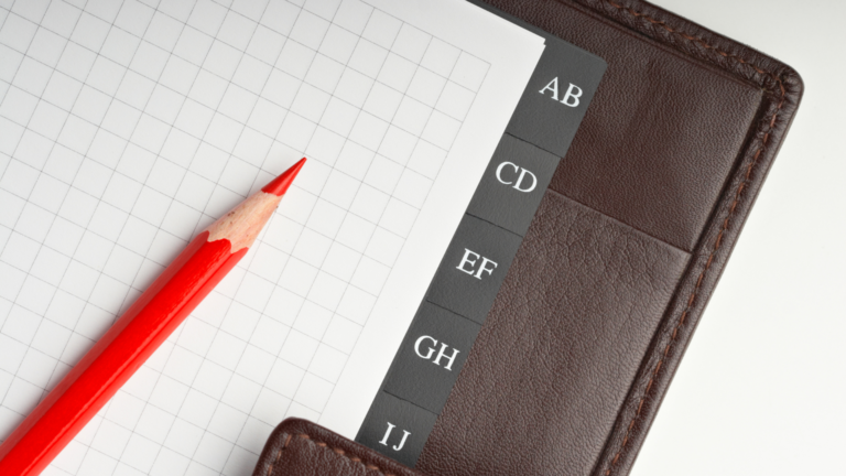 Stylo rouge posé sur des feuilles quadrillées avec onglets noirs pour l'organisation alphabétique