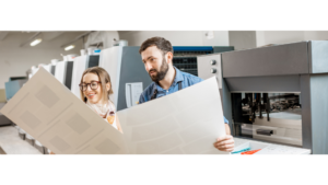 Deux employés vérifiant des impressions près d'une machine dans un atelier d'imprimerie