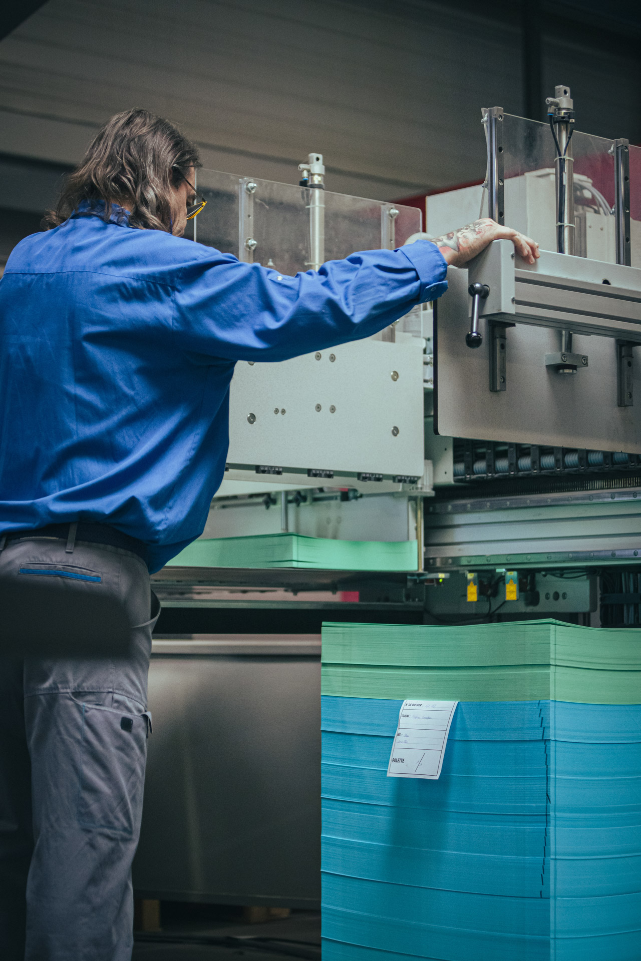 Employé en bleu surveillant une pile de papiers verts dans une machine de découpe